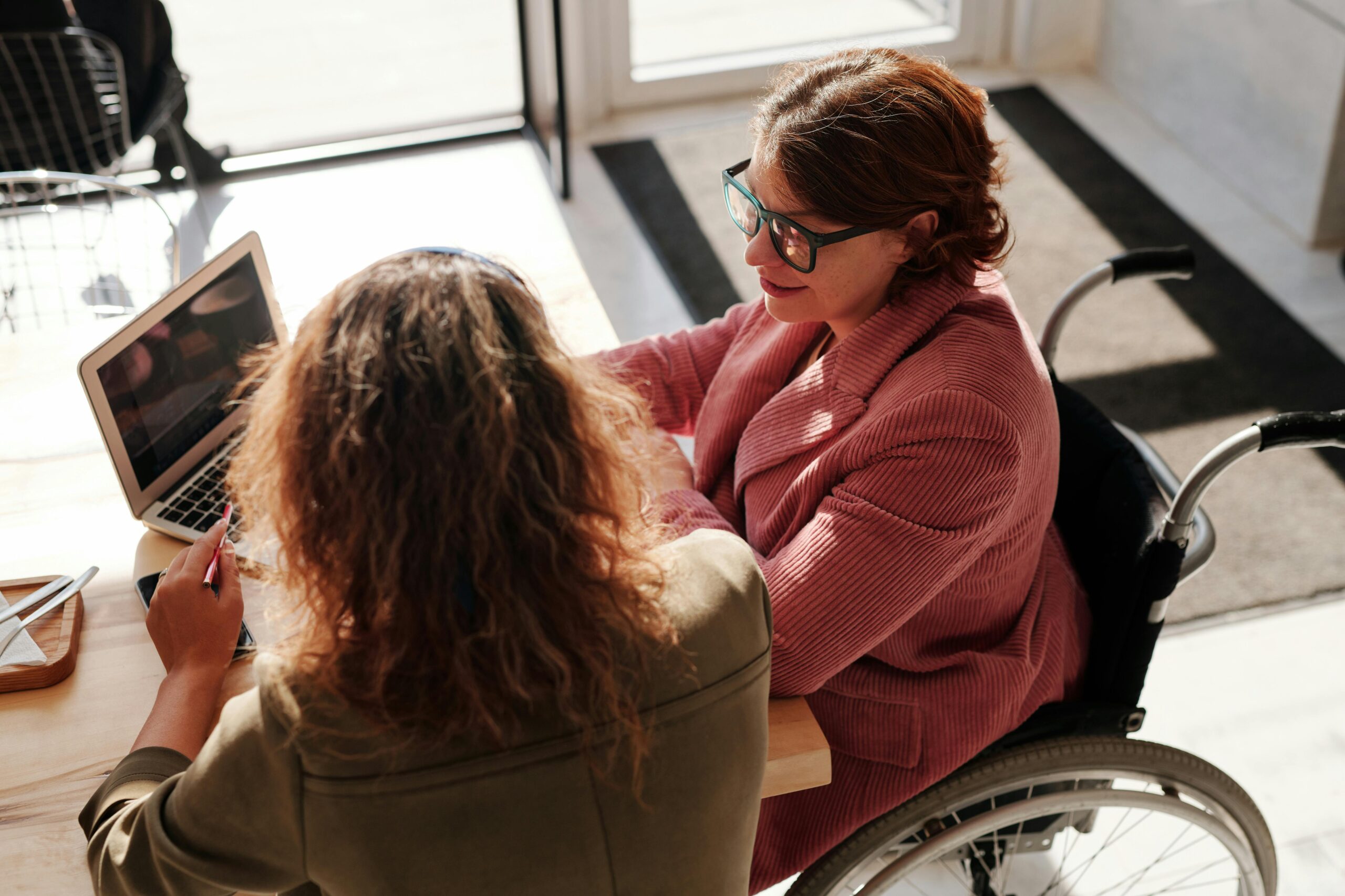 two women sitting at table looking at computer